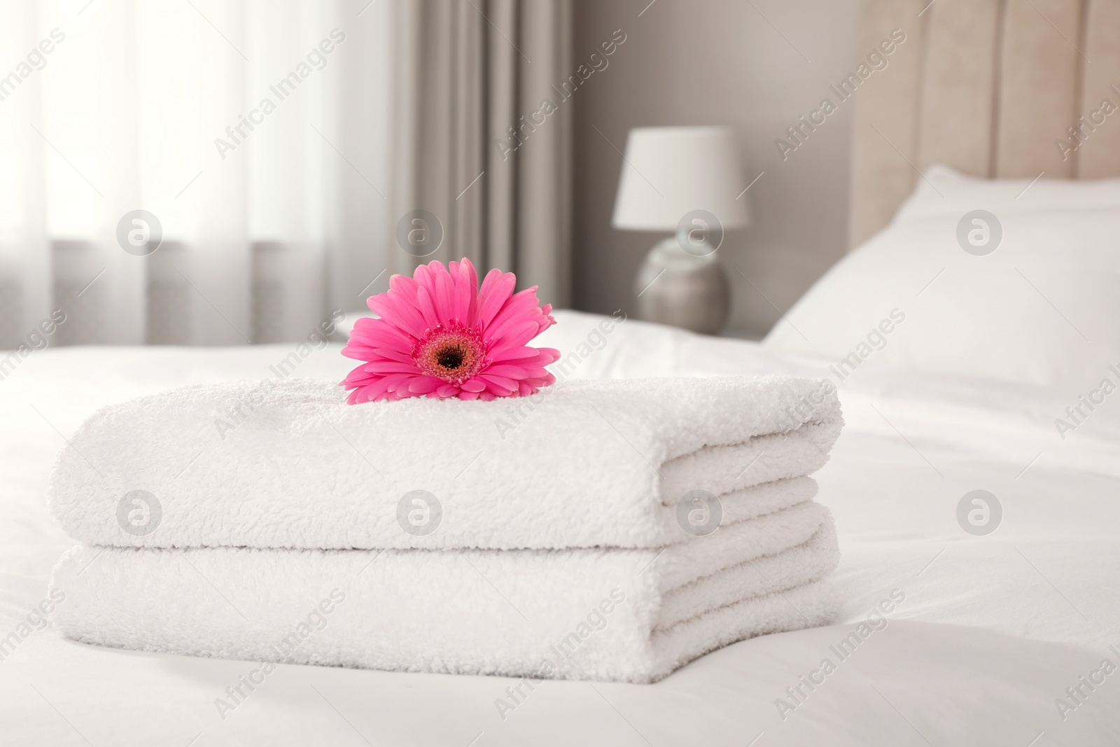 Photo of Stack of fresh towels with flower on bed indoors