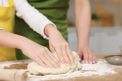 Photo of Making bread. Mother and her daughter kneading dough at wooden table in kitchen, closeup