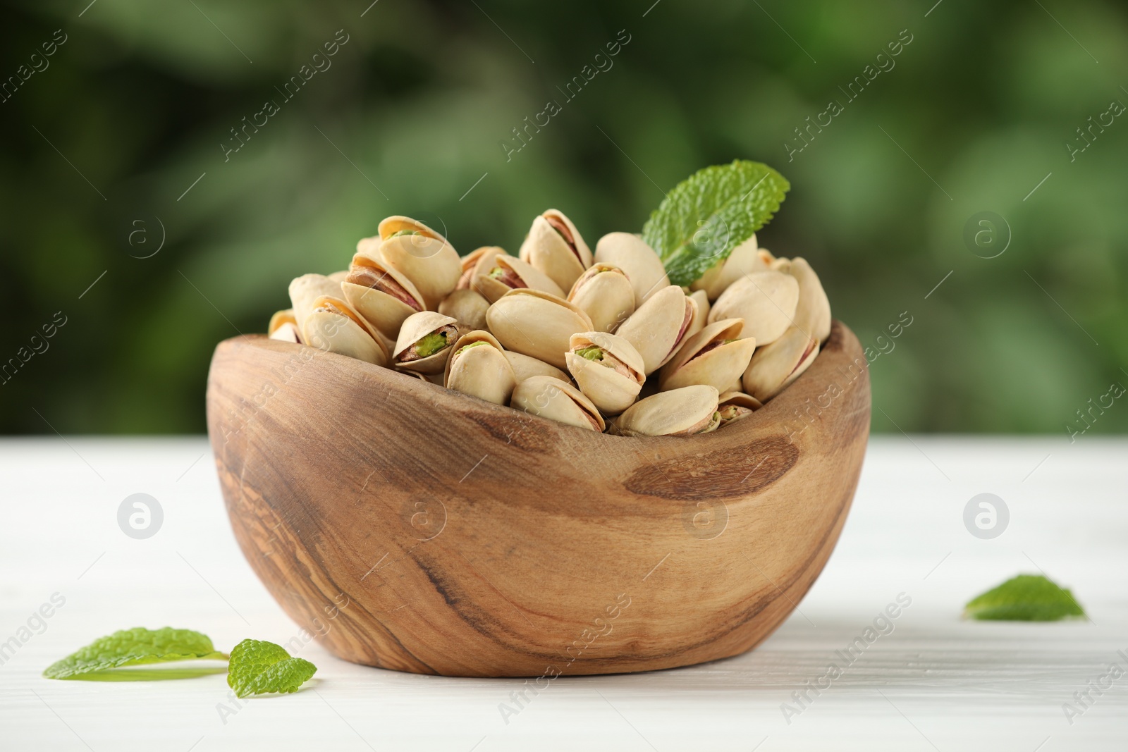 Photo of Tasty pistachios in bowl on white table against blurred background