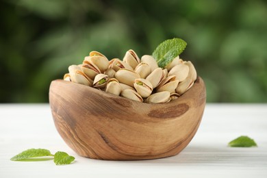 Photo of Tasty pistachios in bowl on white table against blurred background