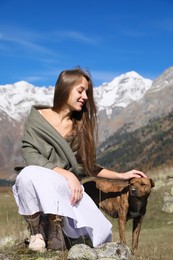 Photo of Beautiful young woman stroking adorable dog in mountains on sunny day