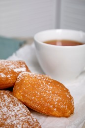 Photo of Delicious madeleine cakes with powdered sugar and tea on table, closeup