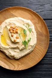 Photo of Bowl of tasty hummus with chickpeas on black wooden table, top view