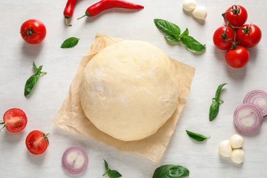 Flat lay composition with dough and fresh ingredients for pizza on white wooden table