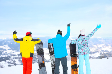 Photo of Friends with snowboards at mountain resort, back view. Winter vacation