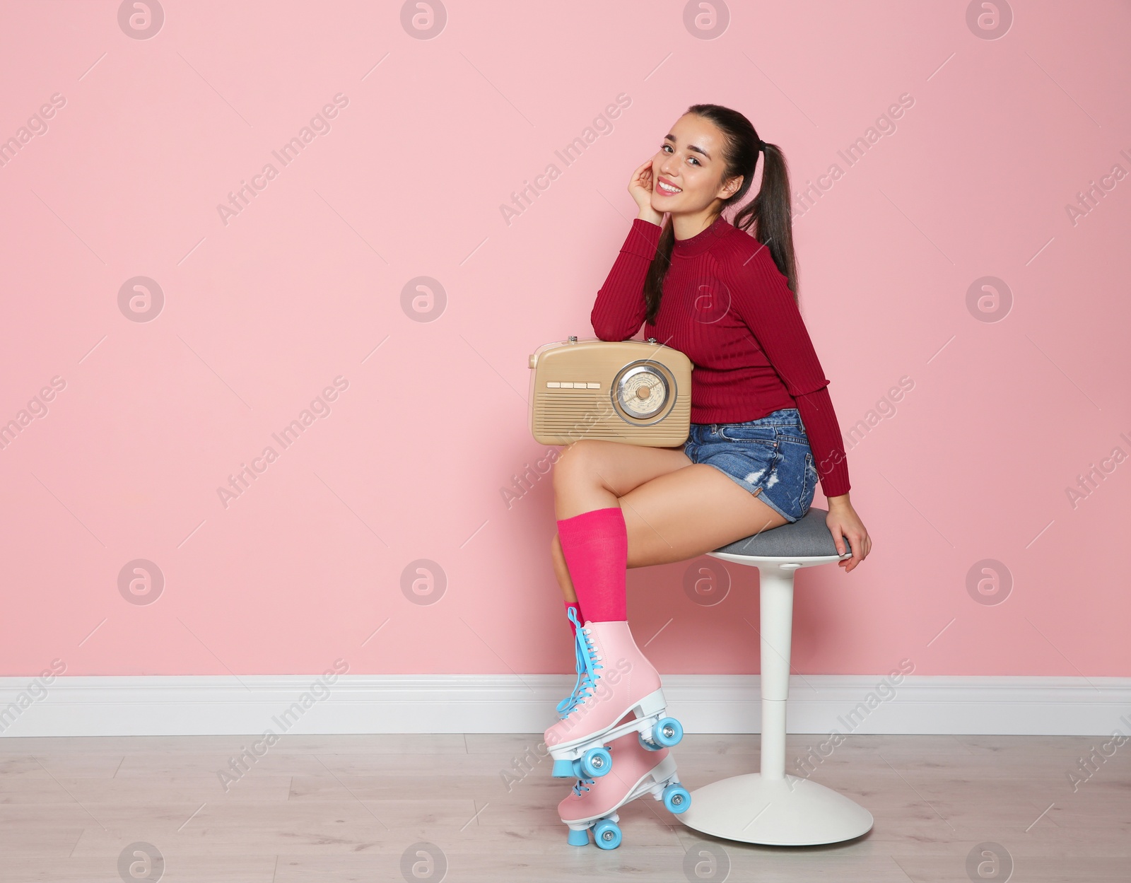 Photo of Young woman with roller skates and retro radio sitting on chair near color wall. Space for text