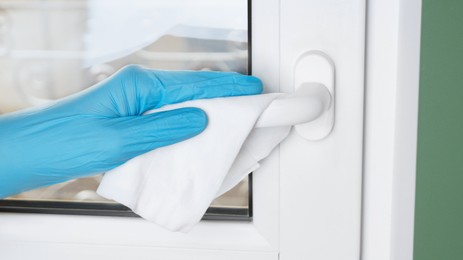 Photo of Man in latex gloves cleaning window handle with wet wipe indoors, closeup. Protective measures