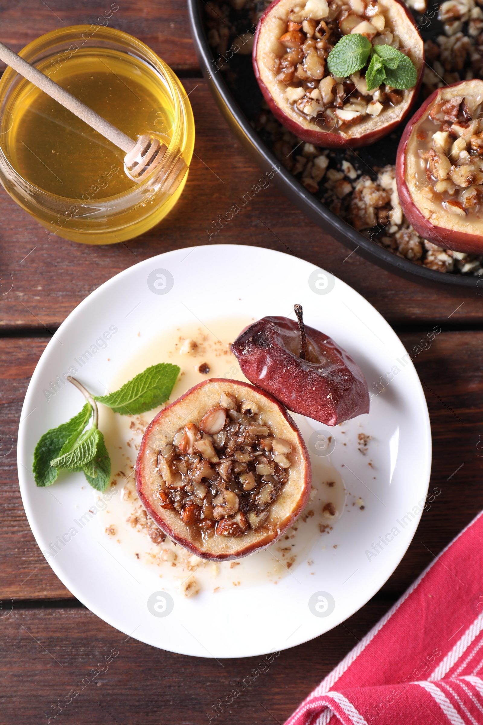 Photo of Tasty baked apples with nuts, honey and mint in dishware on wooden table, flat lay