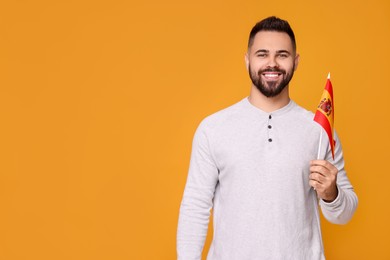 Young man holding flag of Spain on orange background, space for text