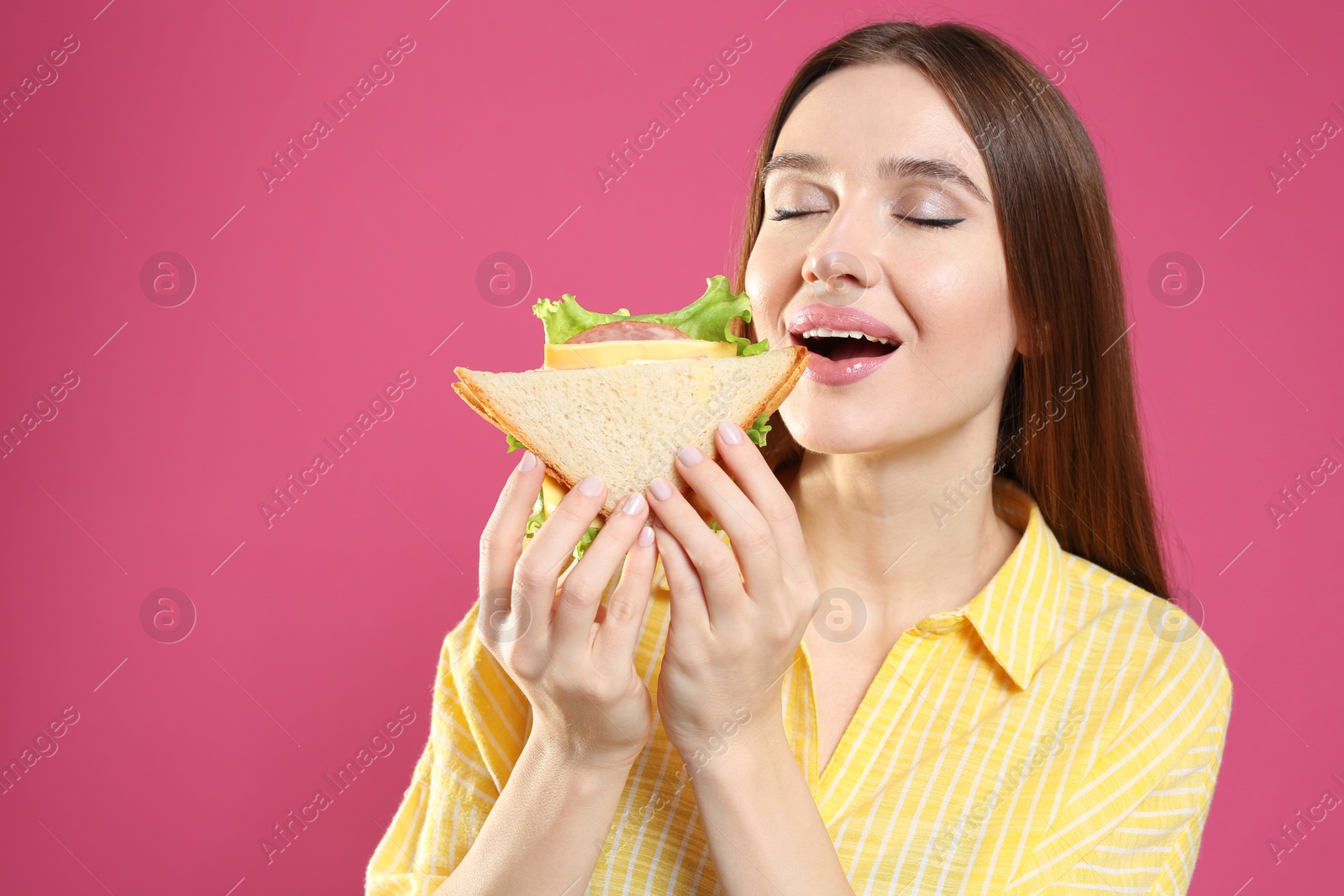 Photo of Young woman eating tasty sandwich on pink background