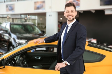 Photo of Young businessman standing near auto in salon. Buying new car