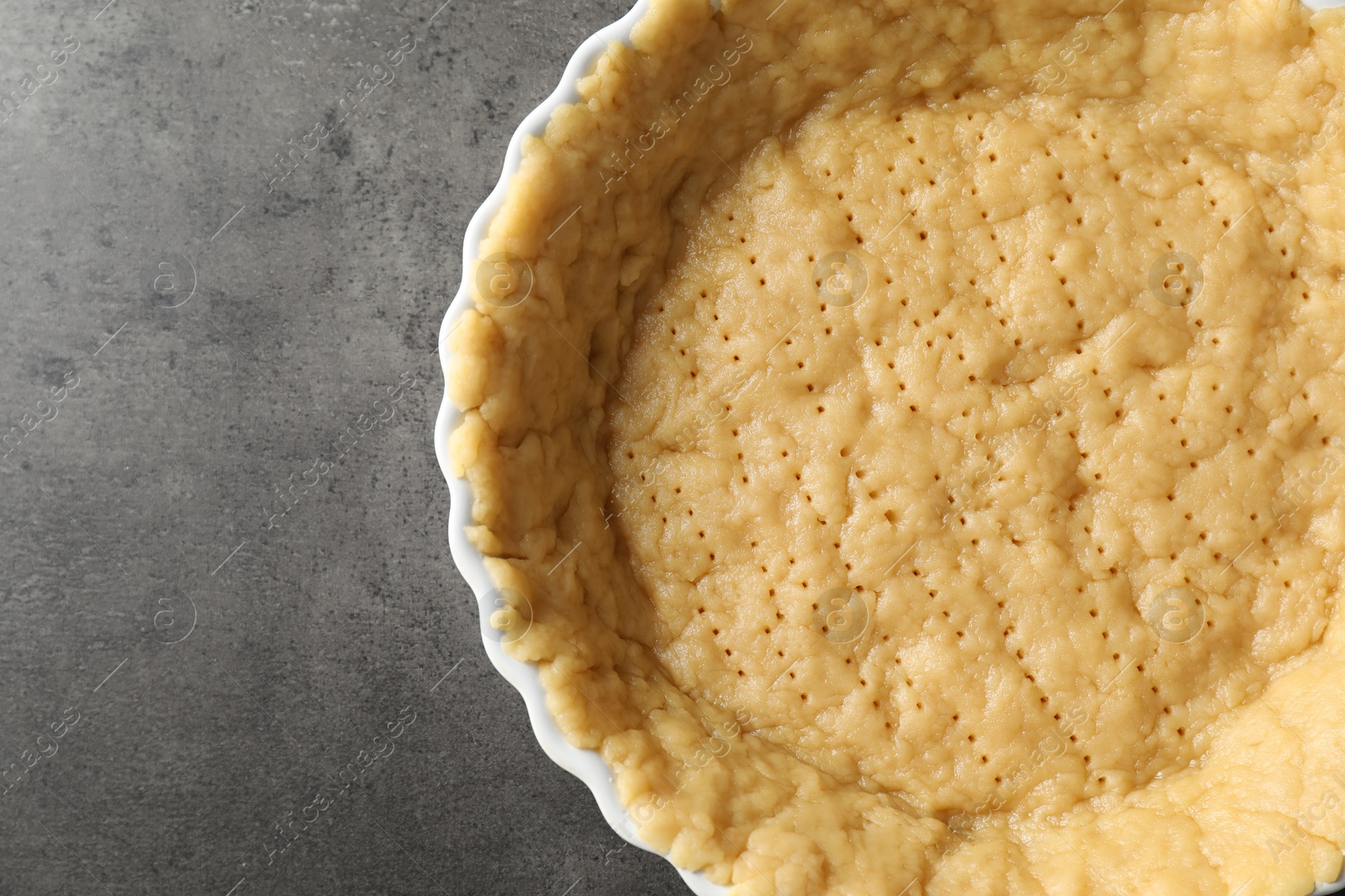 Photo of Making shortcrust pastry. Raw dough in baking dish on grey table, top view. Space for text