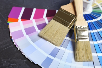 Photo of Brushes and paint color palette samples on gray background, closeup
