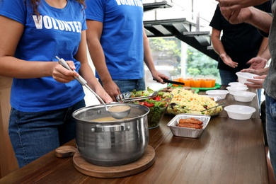 Photo of Volunteers serving food to poor people in charity centre, closeup