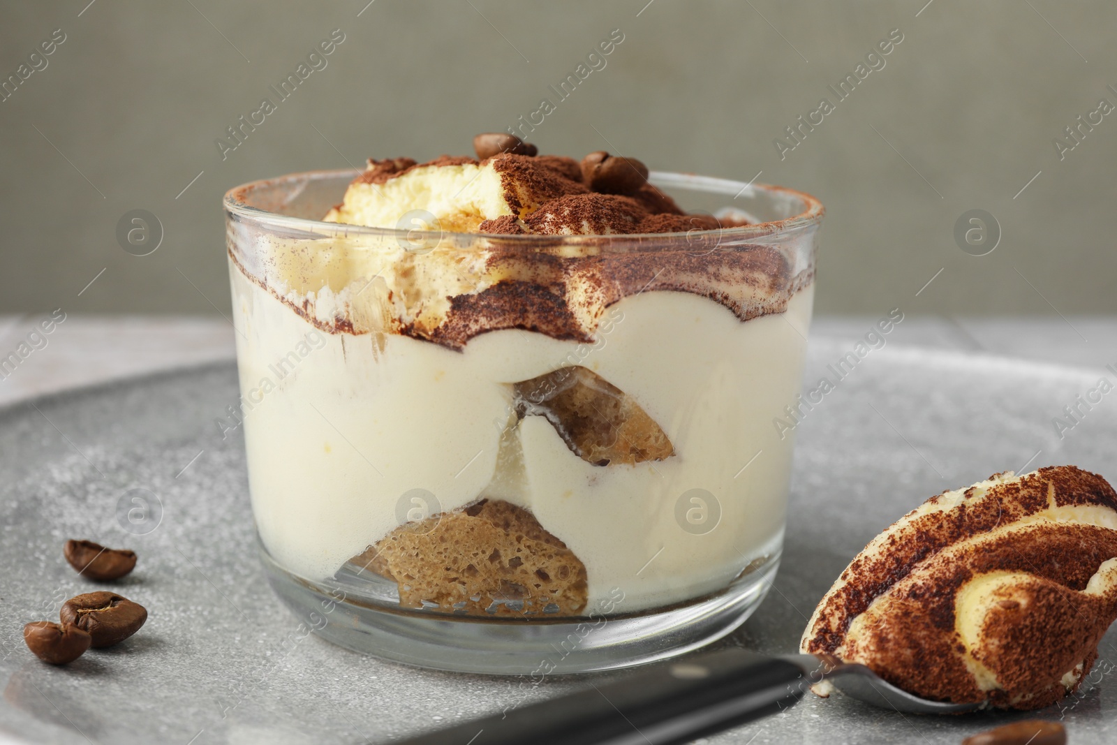 Photo of Delicious tiramisu in glass, coffee beans and spoon on table, closeup