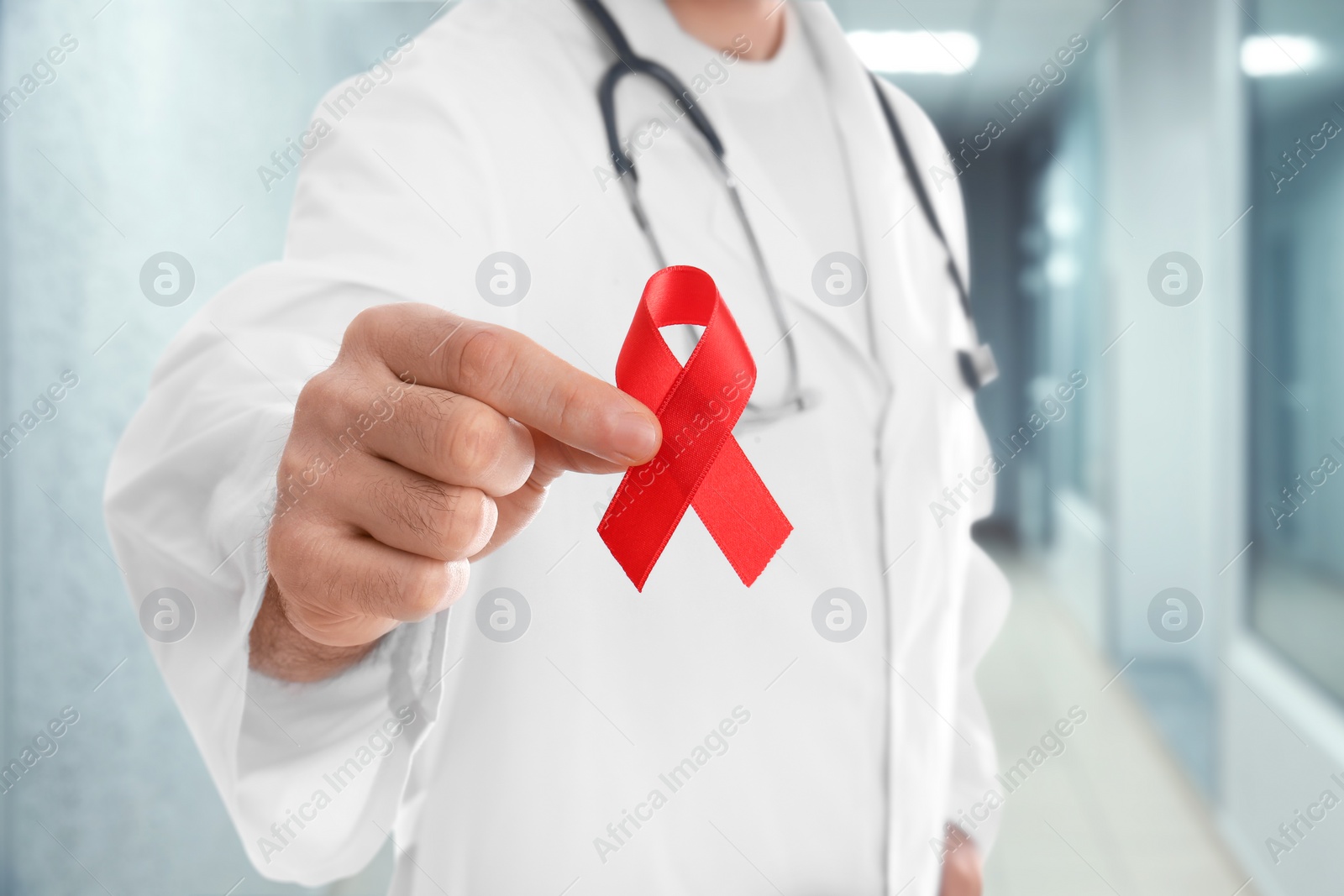 Image of Cancer awareness. Doctor holding red ribbon on blurred background, closeup