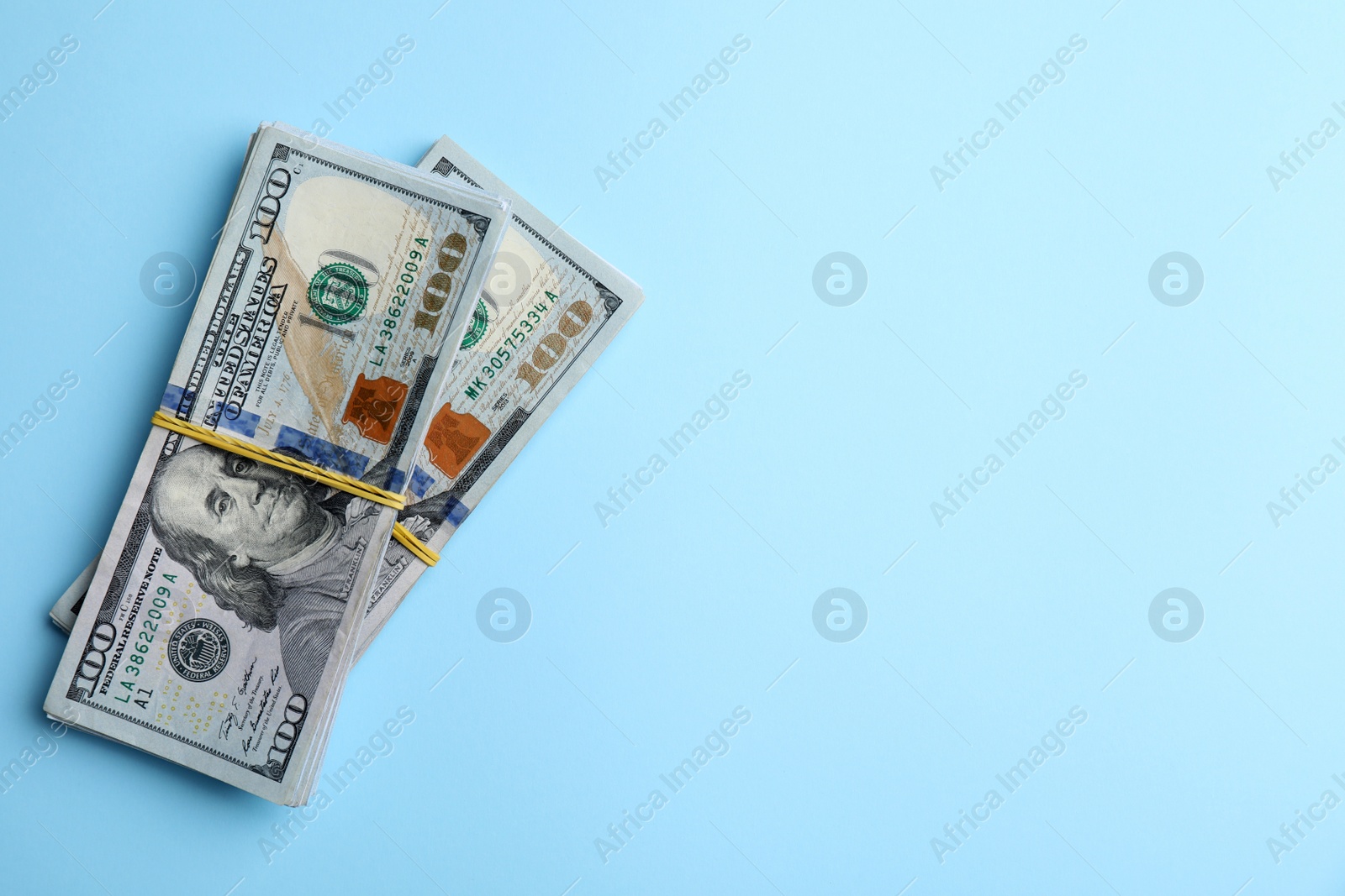 Photo of Bundles of dollar banknotes on light blue background, top view. Space for text