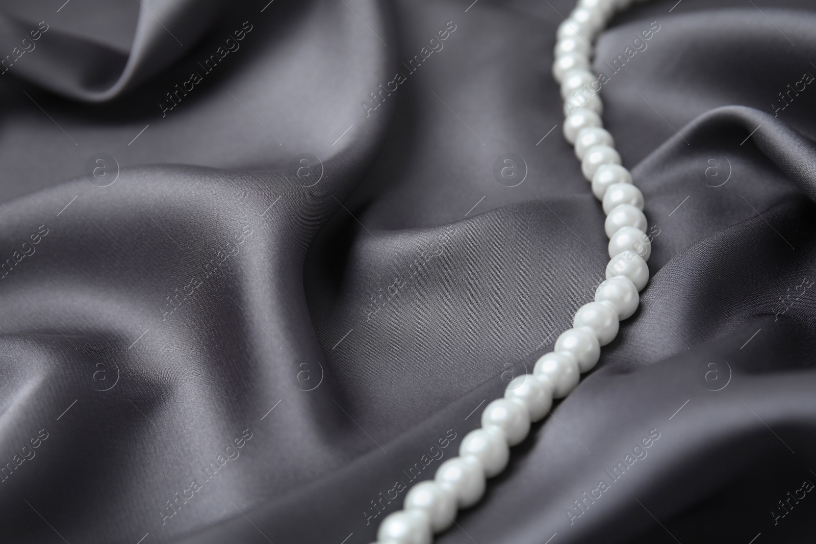 Photo of Beautiful pearls on grey silk, closeup. Space for text