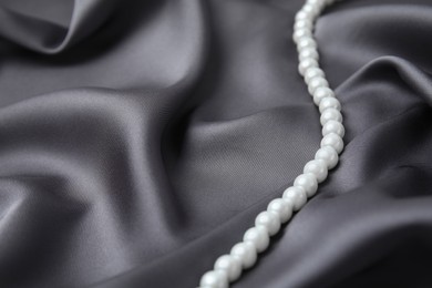 Beautiful pearls on grey silk, closeup. Space for text