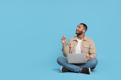 Photo of Smiling young man with laptop on light blue background, space for text