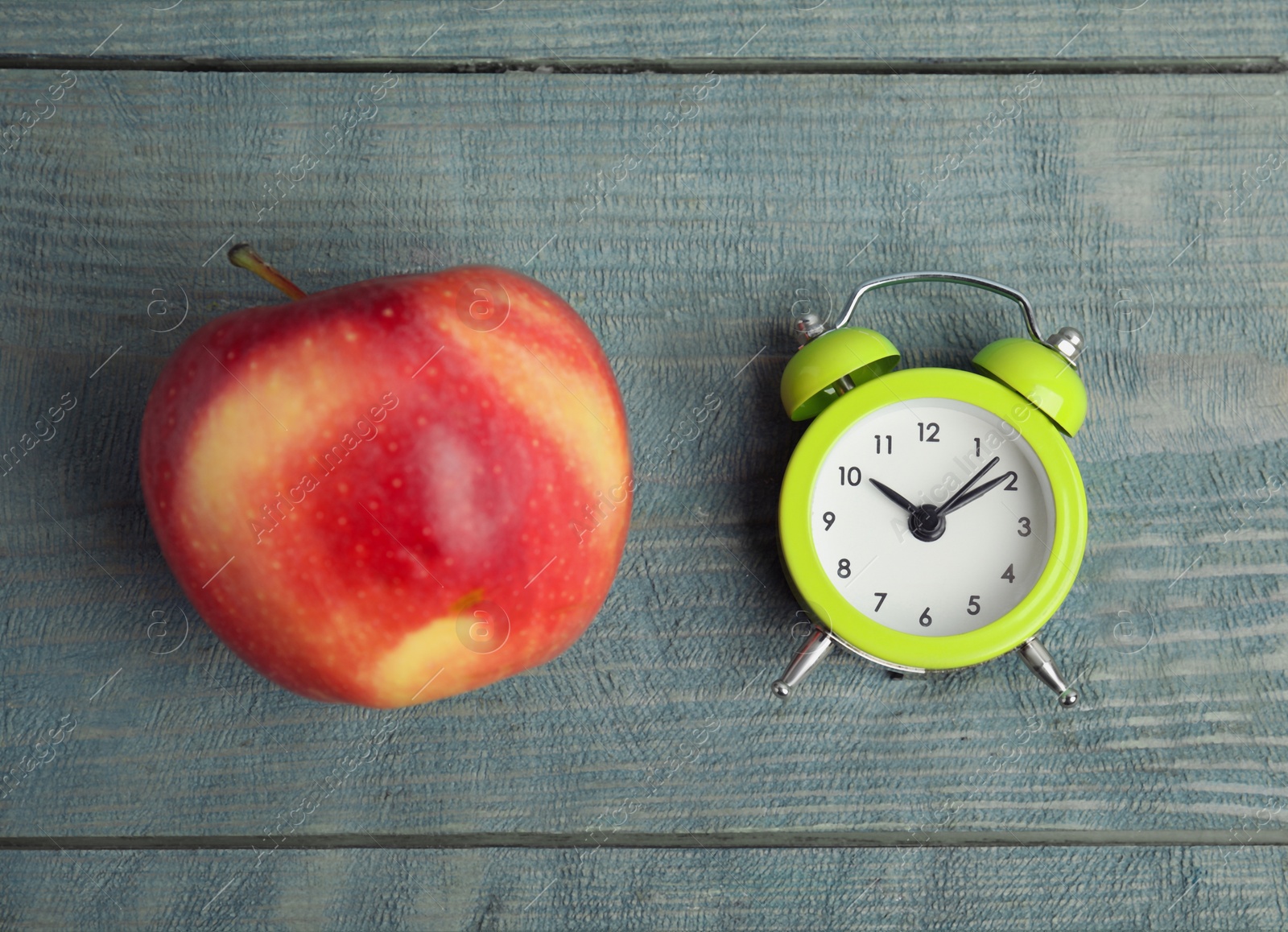 Photo of Alarm clock and apple on light blue wooden table, flat lay. Meal timing concept