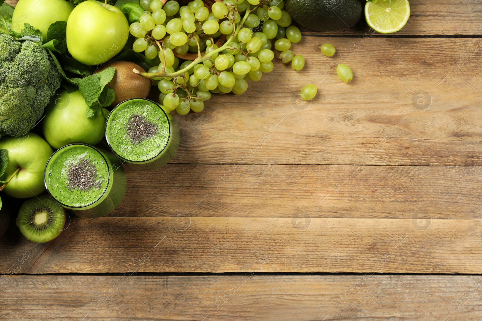 Photo of Glasses of fresh green smoothie and ingredients on wooden table, flat lay. Space for text