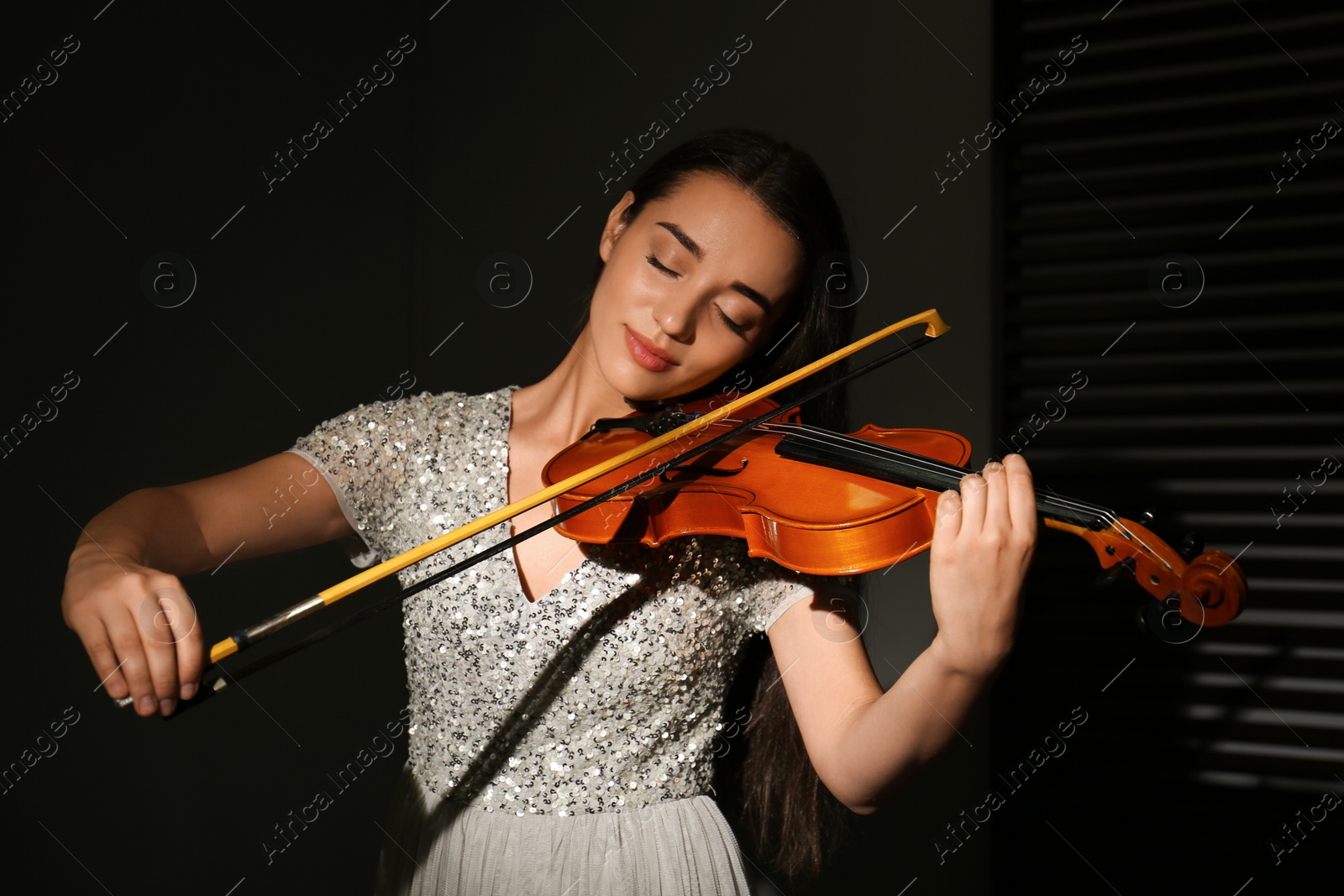 Photo of Beautiful young woman playing violin in dark room