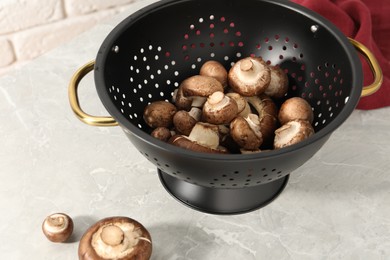 Raw mushrooms in black colander on marble table