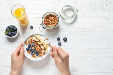 Woman eating tasty yogurt with oatmeal, banana and blueberries at white wooden table, top view. Space for text