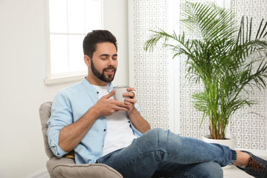 Photo of Young man with cup of drink relaxing at home