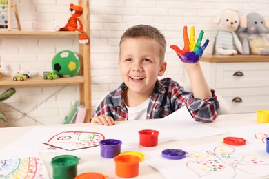Photo of Happy little boy showing painted palm at white table in room