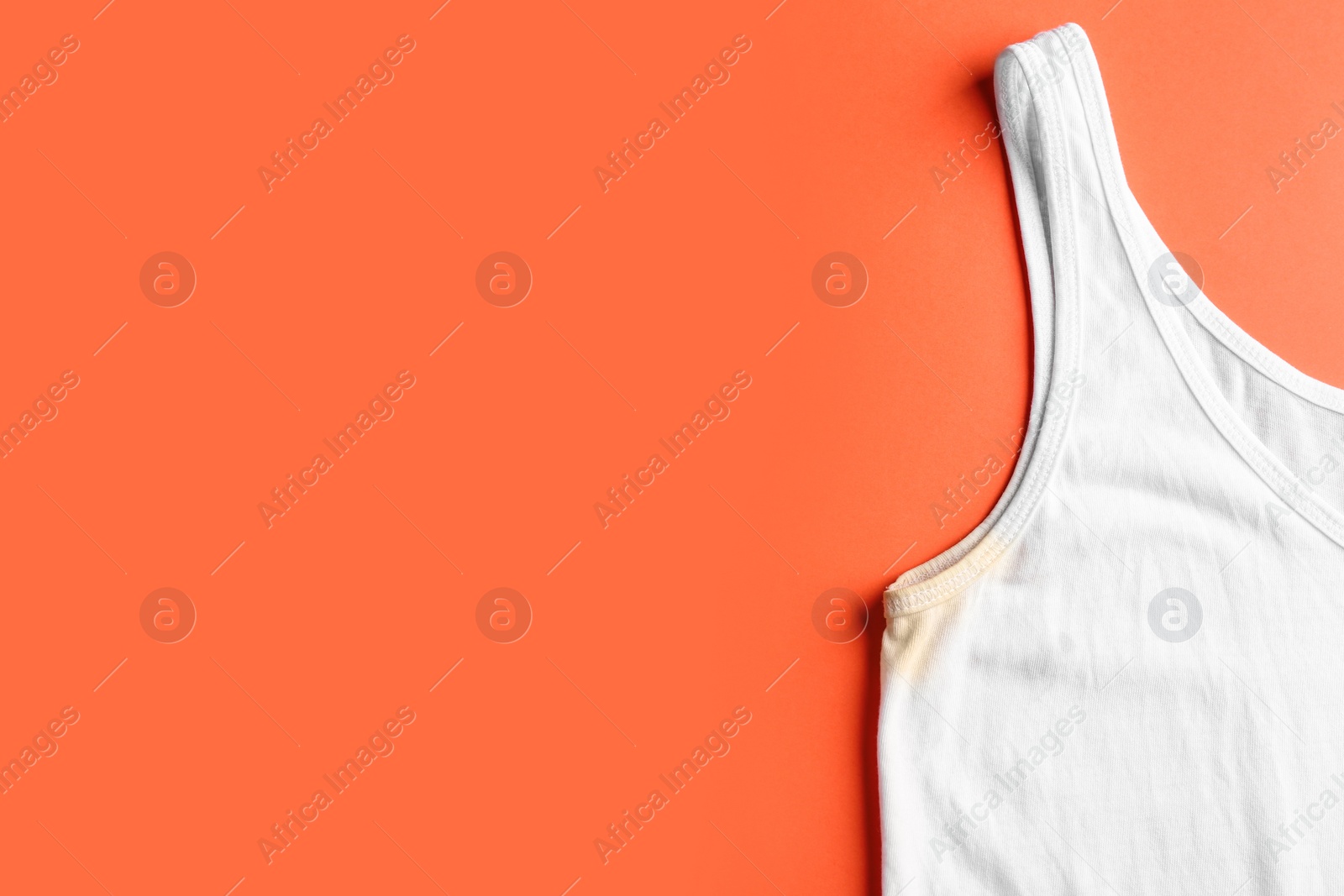 Photo of Undershirt with deodorant stain on coral background, top view. Space for text