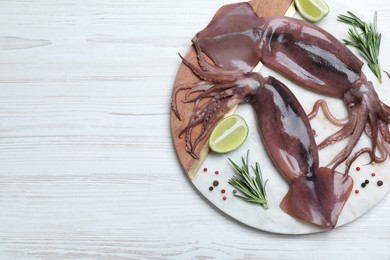 Photo of Fresh raw squids with lime and rosemary on white wooden table, top view. Space for text