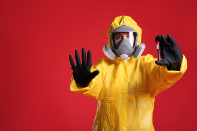 Photo of Woman in chemical protective suit holding test tube of blood sample on red background, space for text. Virus research
