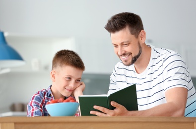 Dad and son reading interesting book in kitchen