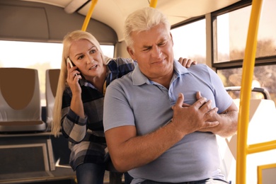 Image of Senior man having heart attack and mature woman calling ambulance to help him in public transport