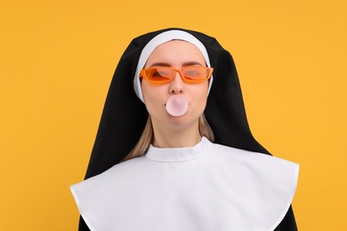 Photo of Woman in nun habit and sunglasses blowing bubble gum against orange background