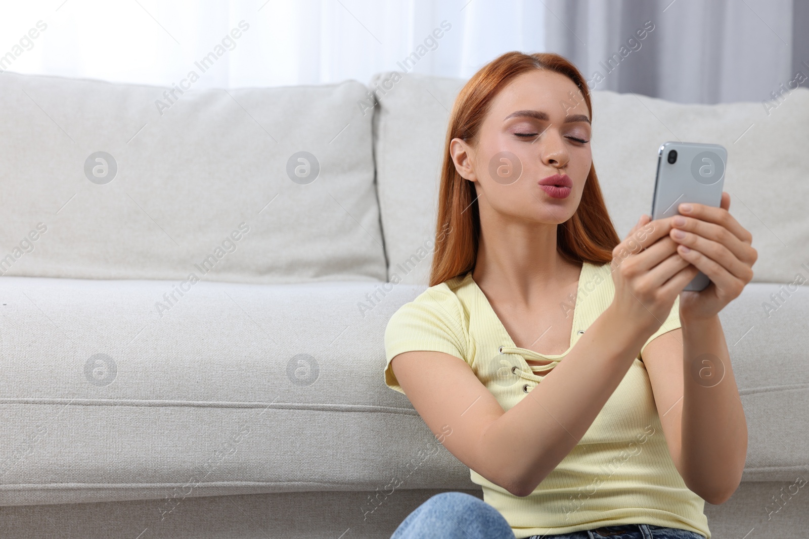 Photo of Happy young woman sending air kiss during video chat via smartphone at home, space for text. Long-distance relationship