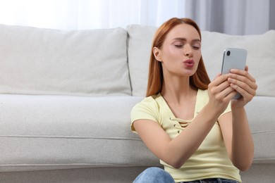 Happy young woman sending air kiss during video chat via smartphone at home, space for text. Long-distance relationship