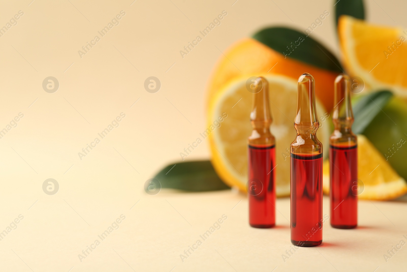 Photo of Skincare ampoules with vitamin C, different citrus fruits and leaves on beige background, closeup. Space for text