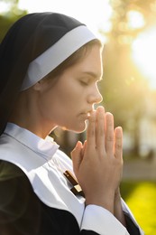 Photo of Young nun with hands clasped together praying outdoors on sunny day