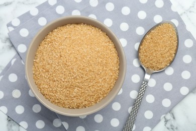 Brown sugar in bowl and spoon on white marble table, top view