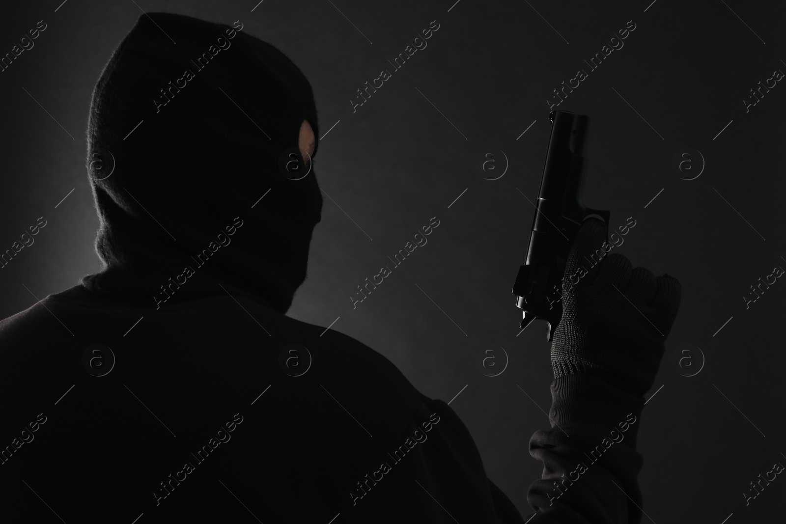 Photo of Dangerous masked criminal with gun on black background. Armed robbery