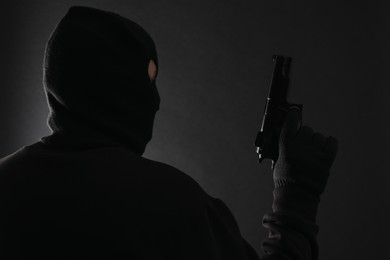Photo of Dangerous masked criminal with gun on black background. Armed robbery