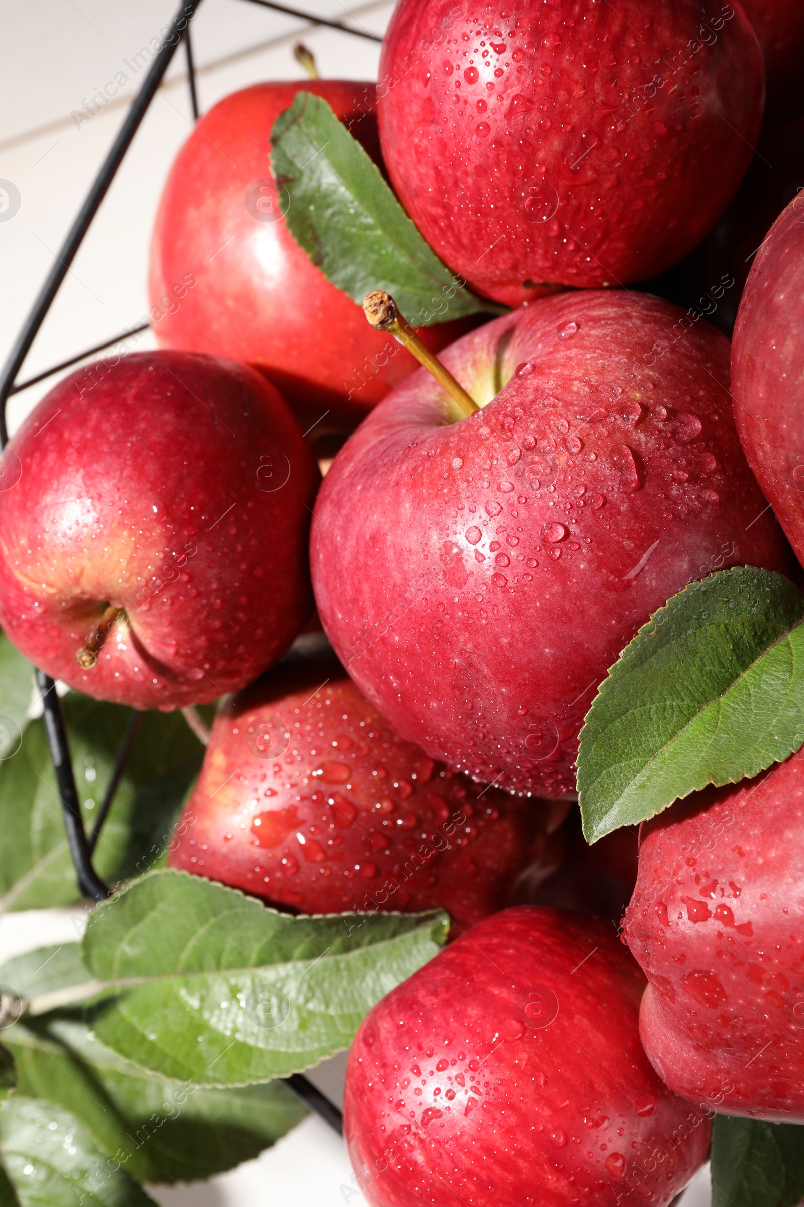 Photo of Ripe red apples with water drops and green leaves on table, closeup