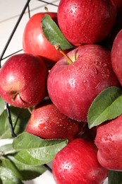 Ripe red apples with water drops and green leaves on table, closeup