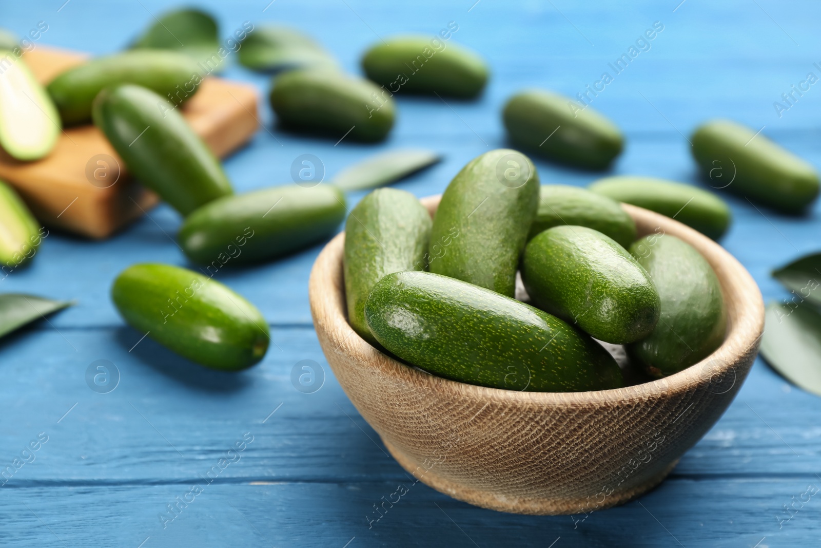 Photo of Fresh seedless avocados in bowl on blue wooden table, closeup