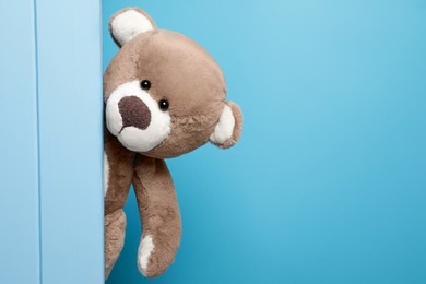 Cute teddy bear behind wooden plank on light blue background, space for text