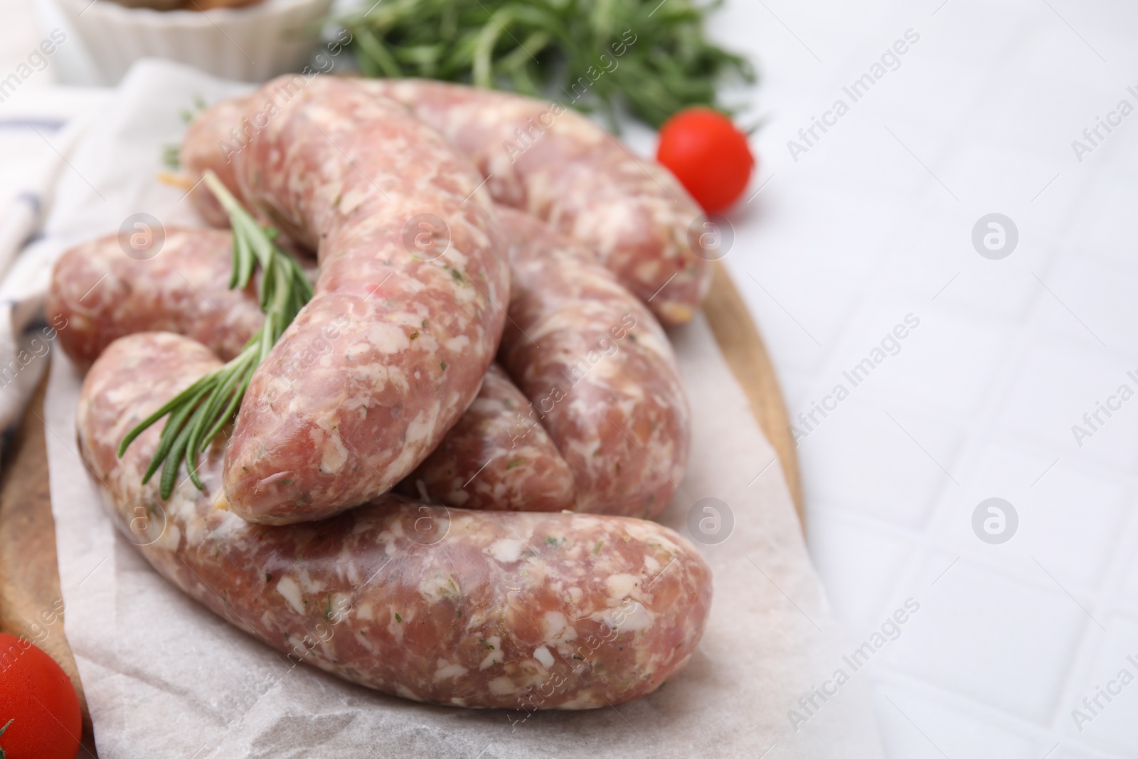Photo of Raw homemade sausages and rosemary on white tiled table, closeup. Space for text