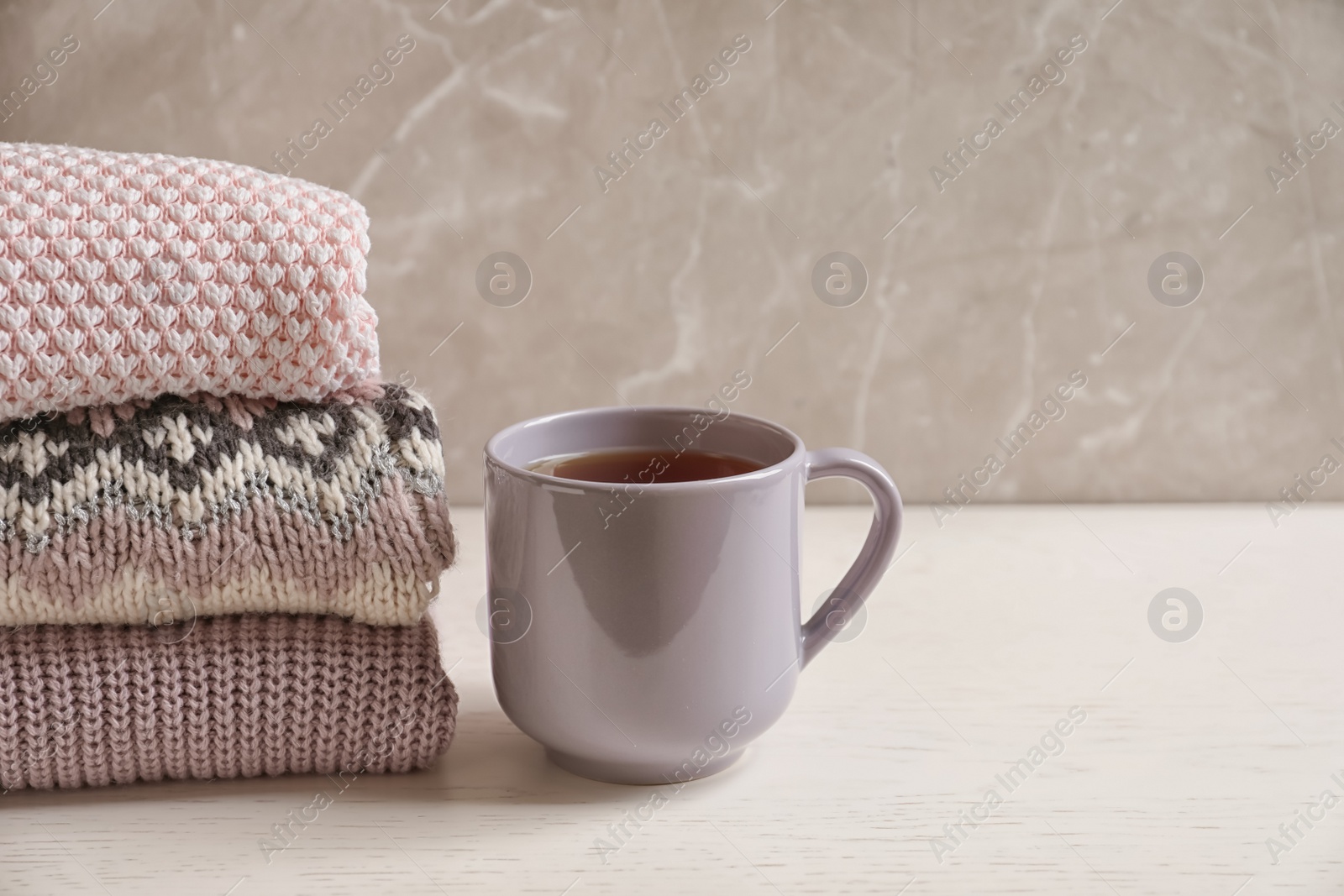 Photo of Stack of warm knitted clothes and cup of tea on table